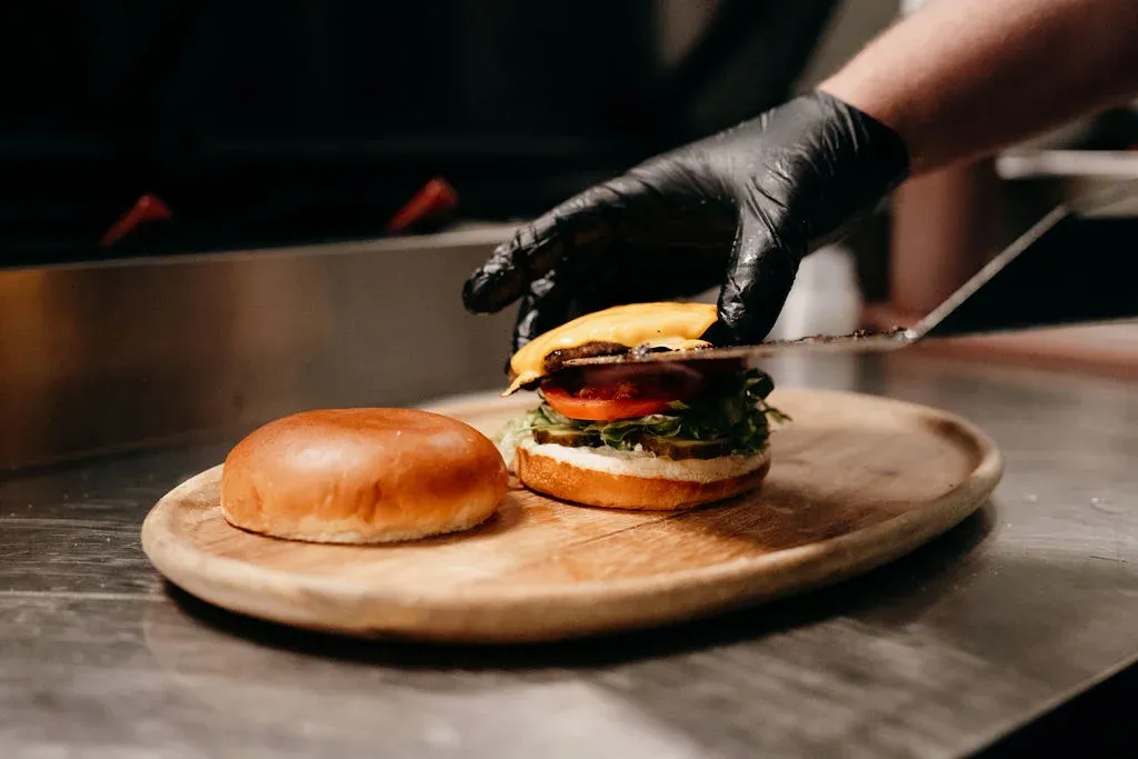 Gloved hand assembling a fresh made cheeseburger.