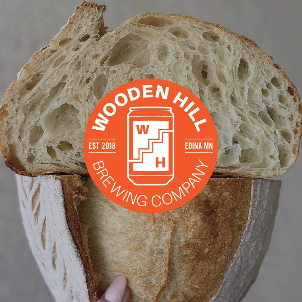 Close-up of rustic sourdough bread, with a sliced loaf showing its airy interior stacked over a whole loaf, overlaid with the Wooden Hill Brewing Company logo.