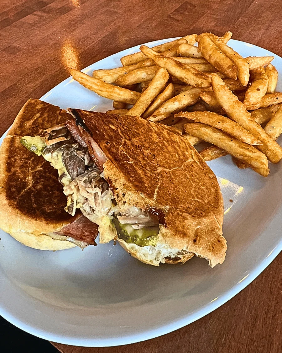 A cubano sandwich cut in half on a plate with a side of fries