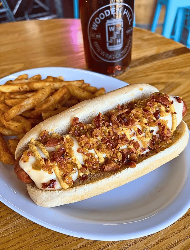 A loaded hot dog called the Dogzilla on a plate with a side of fries
