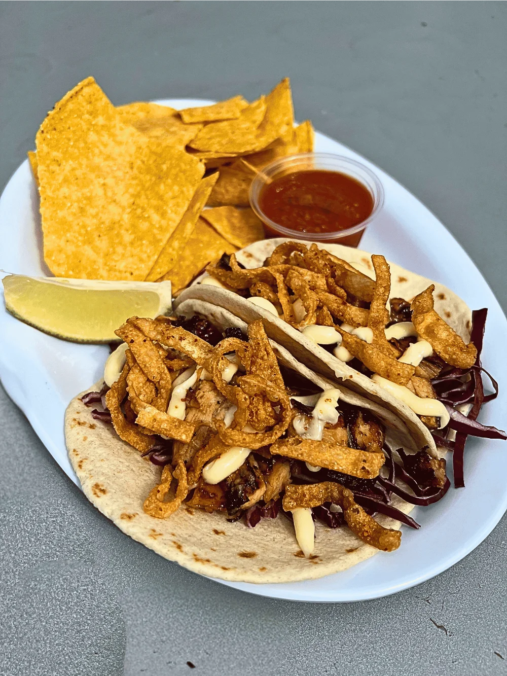a plate of two teriyaki chicken tacos with a side of chips and salsa