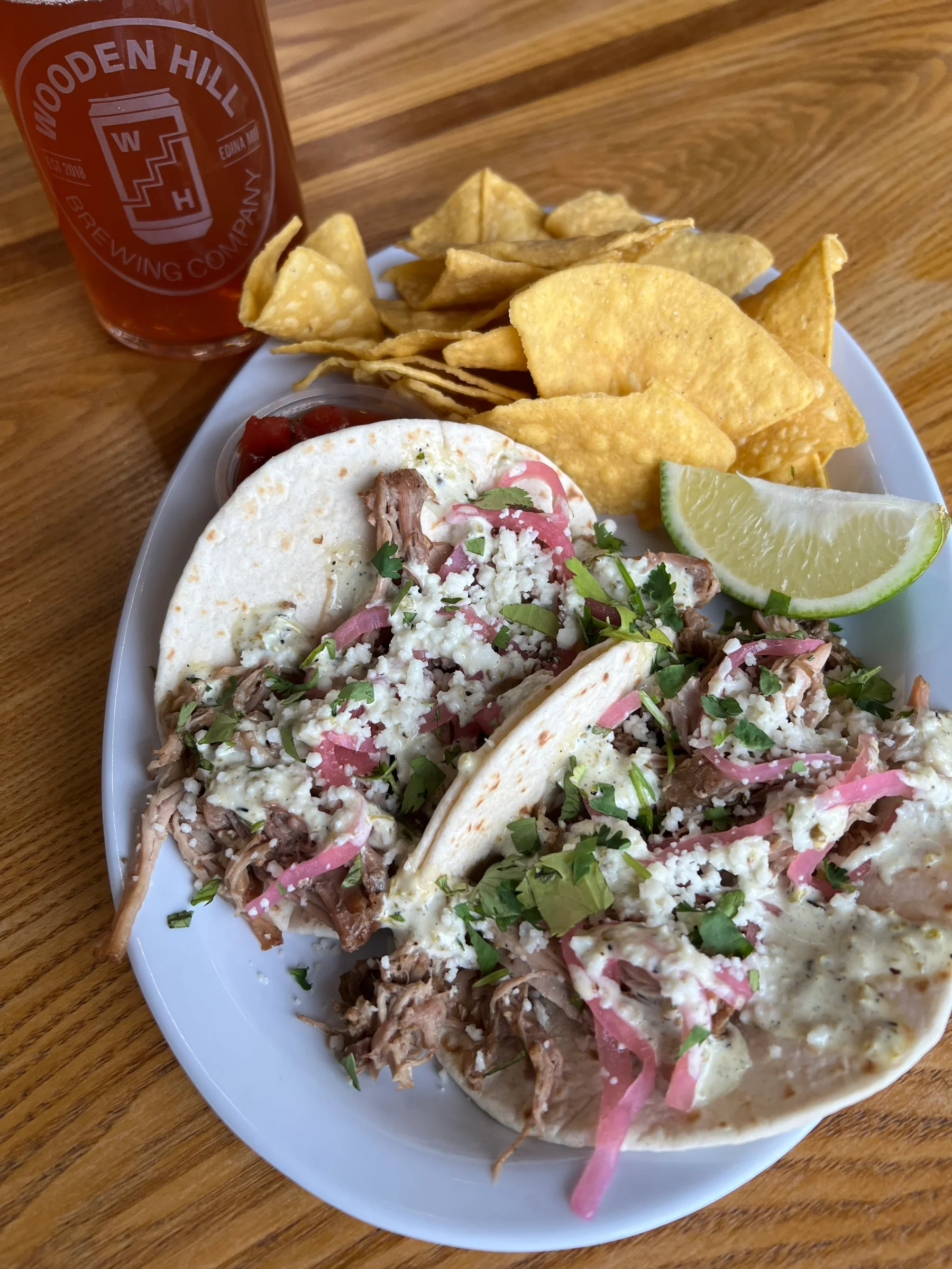 Carnitas tacos on a plate with a side of chips and salsa.