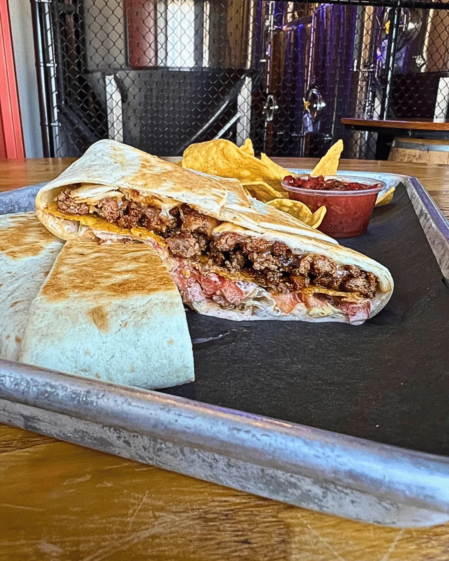 A crunchy wrap cut in half - looking at the inside to see a layer of beef, tostada, cheese, tomatoes, and lettuce.