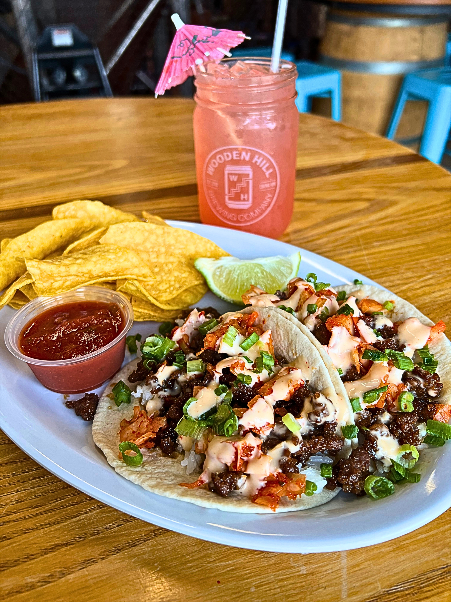 Two Korean beef tacos on a white plate with a side of chips and salsa.