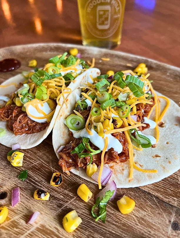 Two soft shell BBQ Pork Tacos on a wooden plate