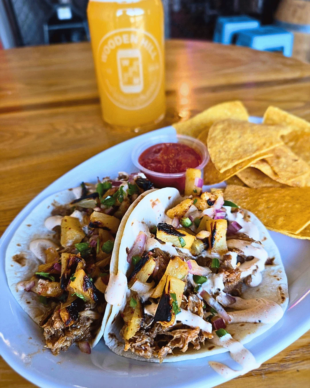 Two chicken tacos with diced pineapple on a plate with a side of chips and salsa
