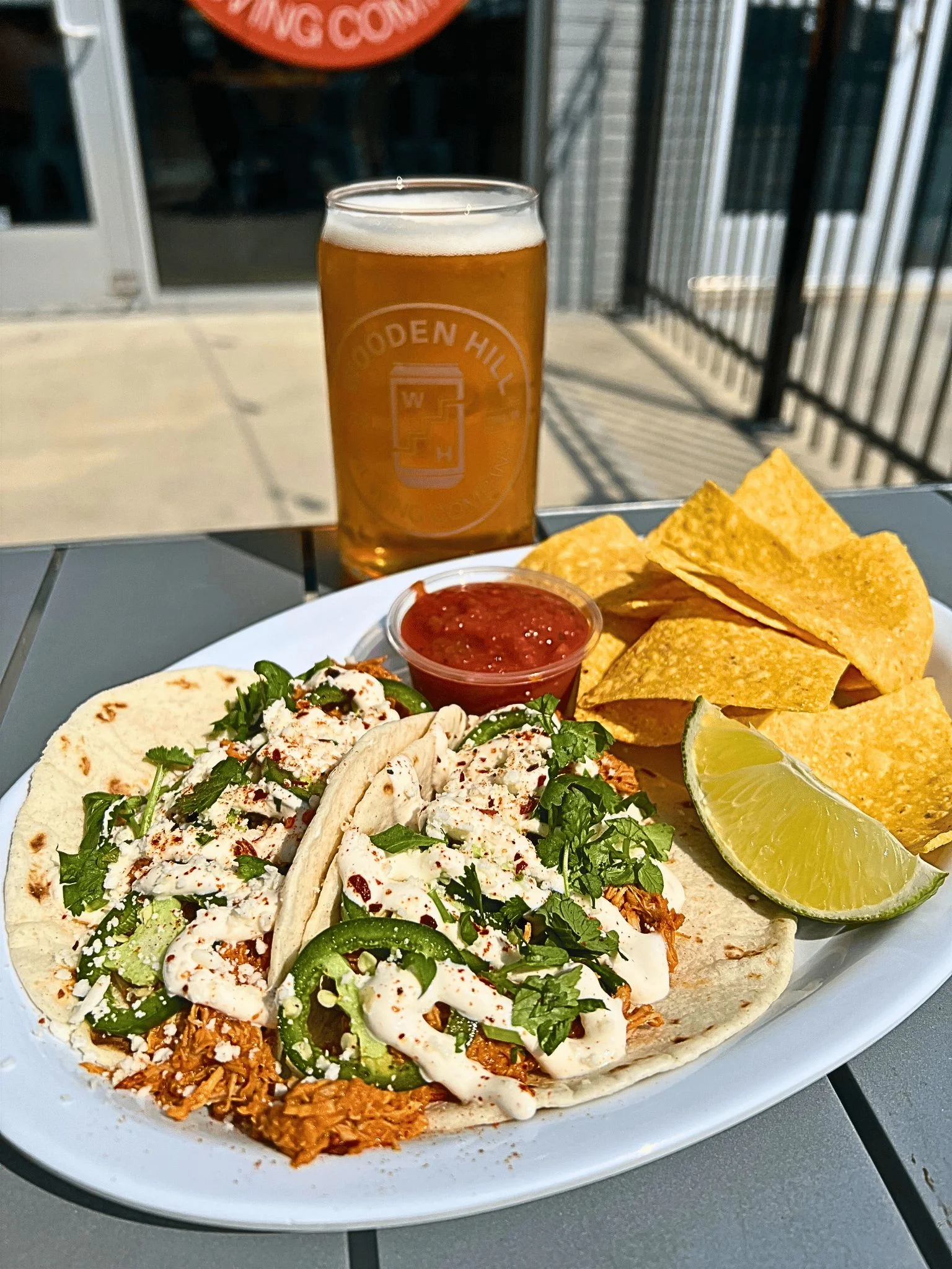 Two loaded tacos served on a plate with tortilla chips, salsa, and a lime wedge.