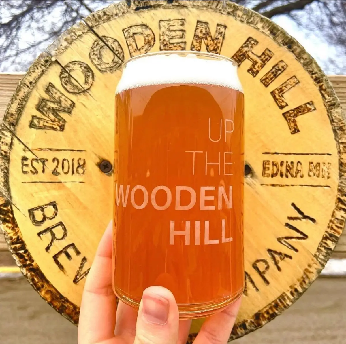 Picture of The Radler cocktail in a glass, in front of our wooden logo on the patio