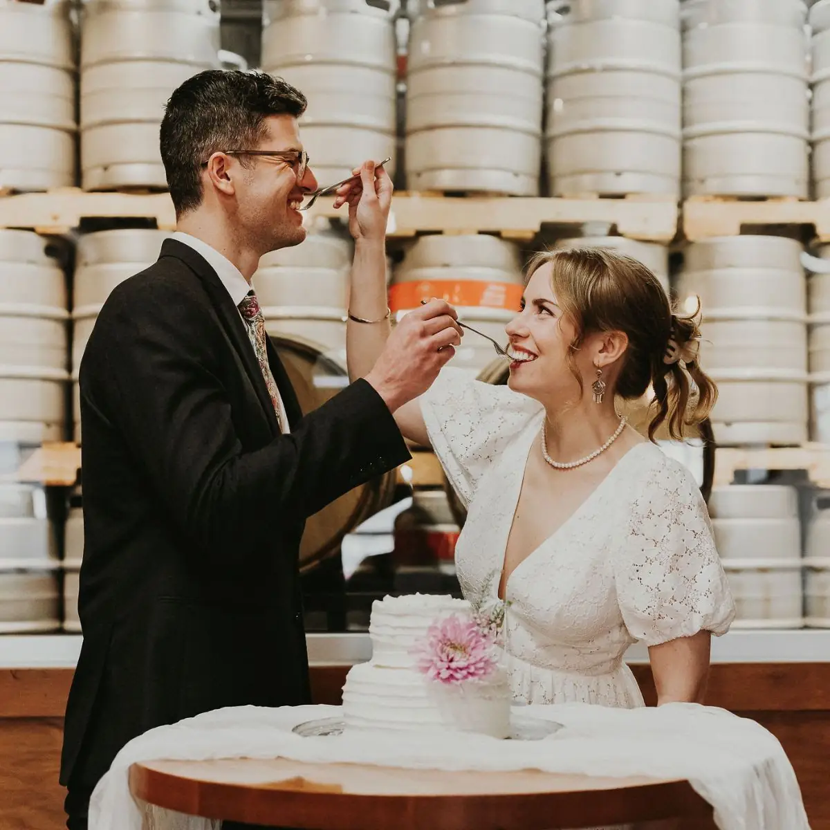 photo of a wedding couple sharing wedding cake in front of wooden hills keg wall