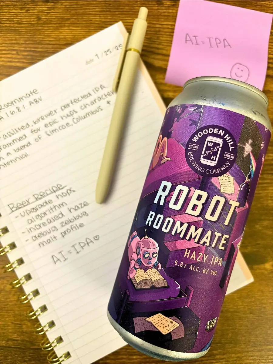 Image focused on Robot Roommate can which is shades of purple of a dorm room with a robot. Background of image has a notebook with writing and a purple post-it note that says AI=IPA with a smiley face and a pen laying on the notebook. All is laying on a wood platform. 