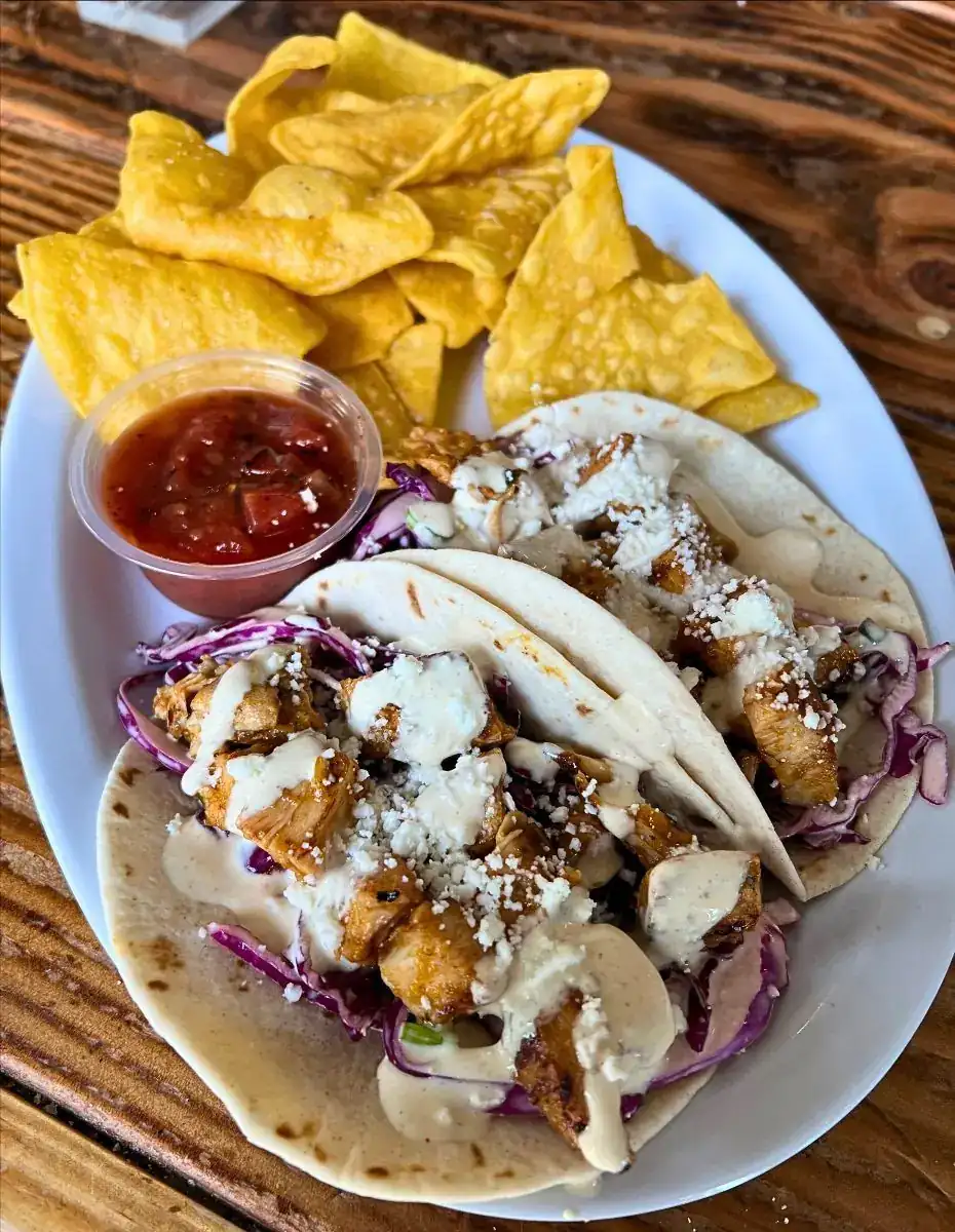 Plate with Kickin' Peach Tacos on it with salsa and chips. Plate is on a wood table. 