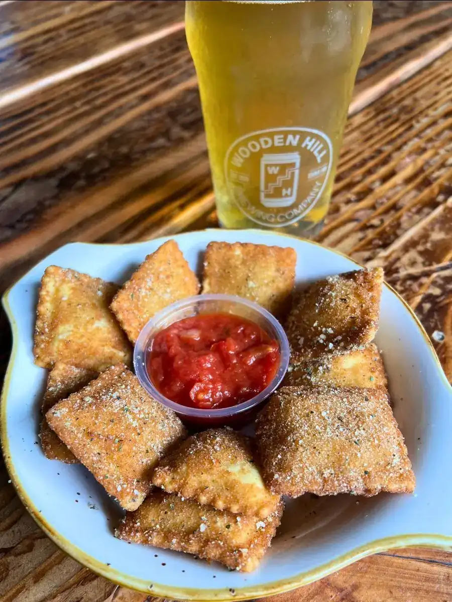 Picture of our new Toasted Ravioli! Picture shows ravioli in a circular dish with marina in the center and a light beer in the background.