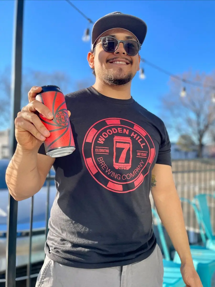 photo of a guy holding a can and wearing a wooden hill 7th anniversary tee