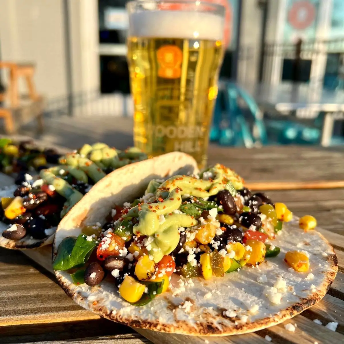 Picture of this week's Taco Wednesday special, Cowboy Caviar Tacos! Picture includes two tacos and a beer in the back.
