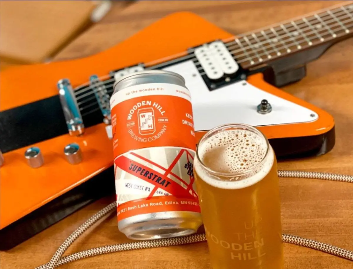 Picture of our returning West Coast IPA, Superstrat, shown in a glass and a crowler can. Also pictured, an orange electric guitar.