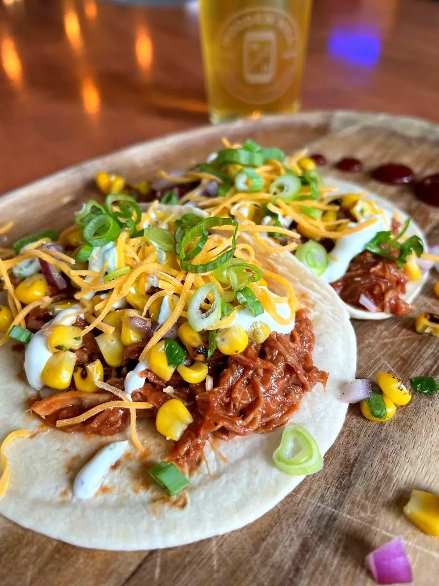 A picture of two BBQ Pork Tacos with a drink on the side.