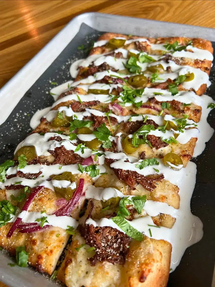 Image of a Birria Flatbread on an aluminum tray with black paper under it.