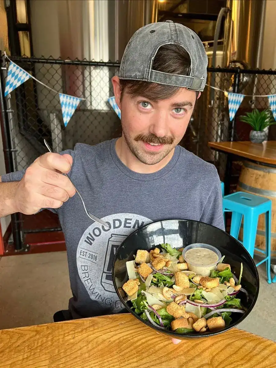 Image of a guy holding a Caesar Salad in one hand and a fork in the other hand.