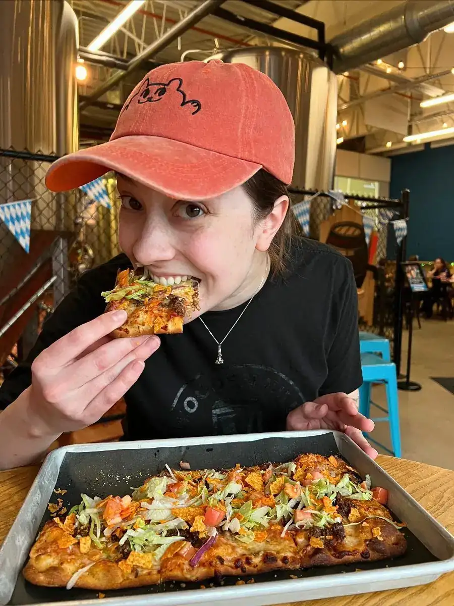 Image of a women eating a slice of flatbread. Fiesta flatbread in front of her on a tray.