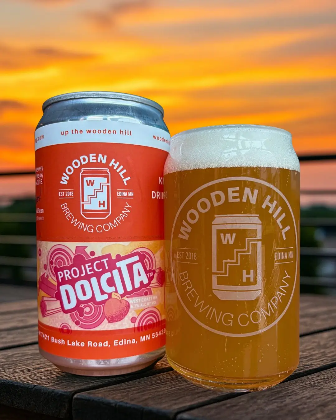 Project Dolcita Wooden Hill beer can and glass of west coast IPA. Sunset in the background and the drinks are on a wood table.