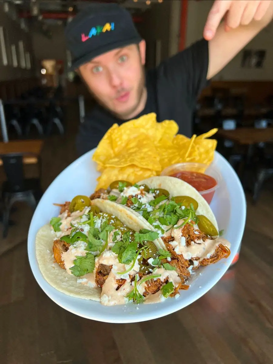 Picture showcasing this week's taco special - Heatwave tacos! Picture shows two tacos on a plate with a side of chips & salsa. Model in background.