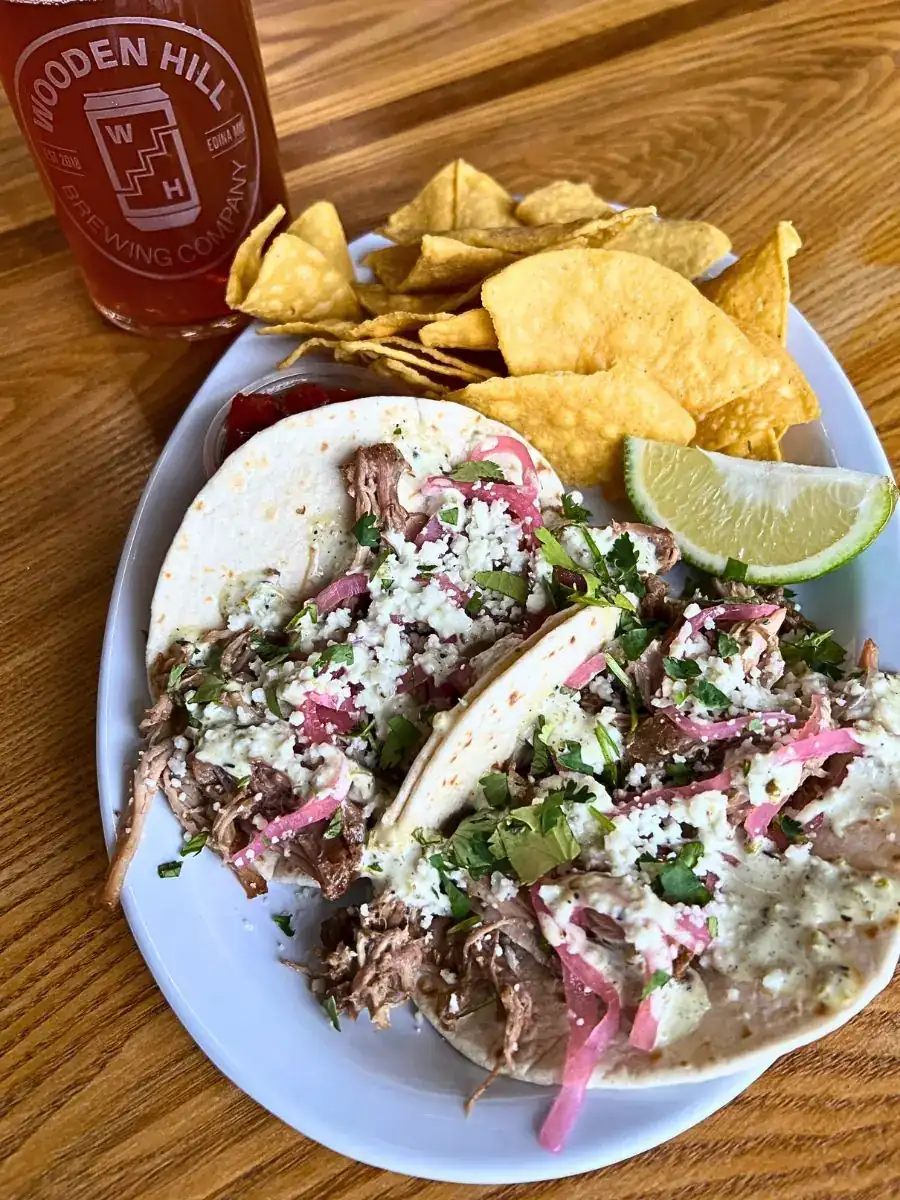 Two soft flour tortillas loaded with shredded pork carnitas, pickled red onion, roasted serrano crema, queso fresco, and fresh cilantro. Served with a lime wedge, side of chips, salsa, and a pint of Wooden Hill beer