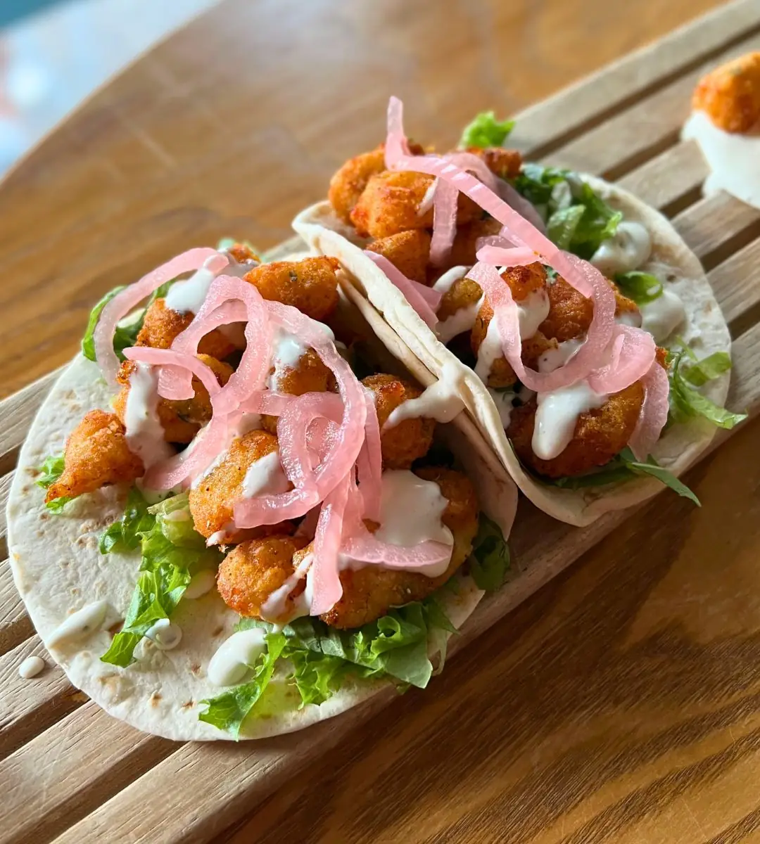 Two mouth-watering cheese curd tacos loaded with crispy golden curds, fresh greens, white crema, and vibrant pickled red onions on soft flour tortillas