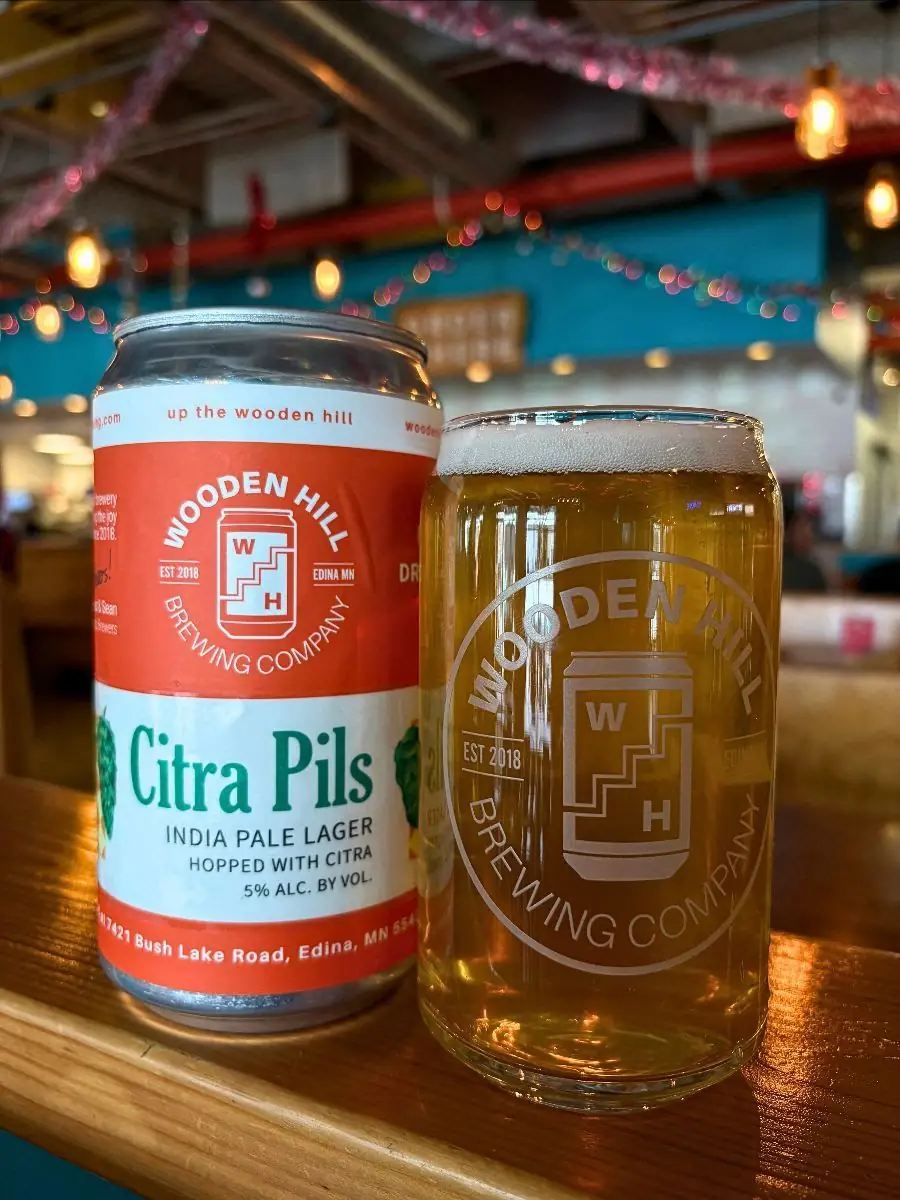Image of a Wooden Hill can with the Citra Pils logo on the left. On the right, a Wooden Hill glass with a lighter beer.