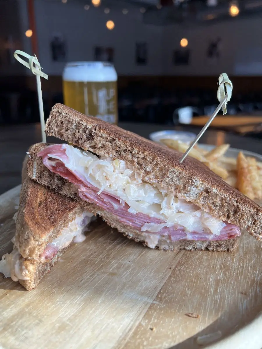 A Ruben sandwich cut in half. Toasted marble rye bread, sliced corned beef, with melted swiss cheese and house sauerkraut