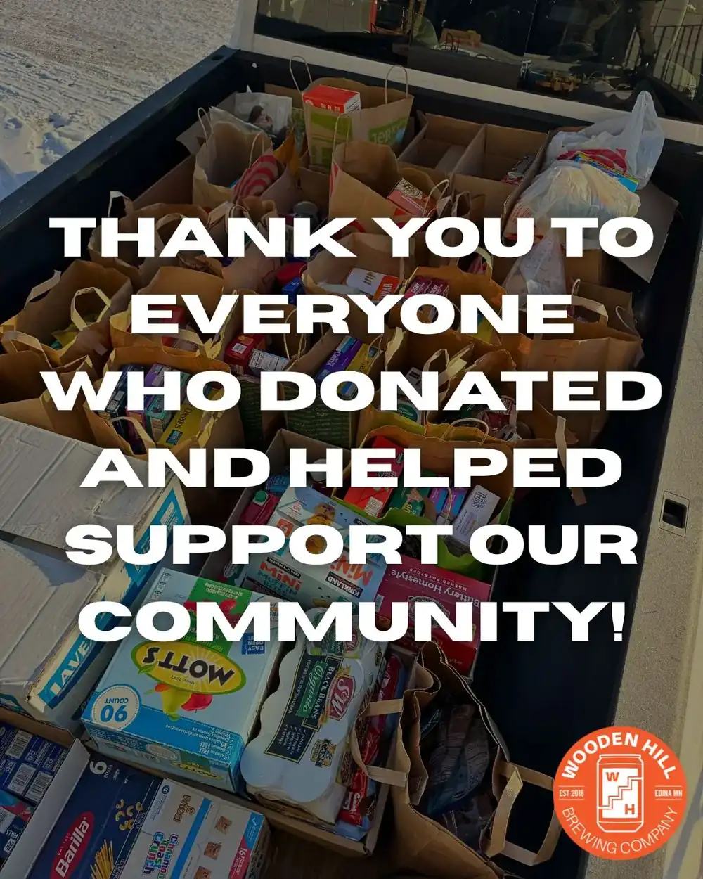 Image of a truck bed filled with food donations in paper bags. Writing over it says "Thank you to everyone who donated and helped support our community", Wooden Hill logo in the bottom right corner.