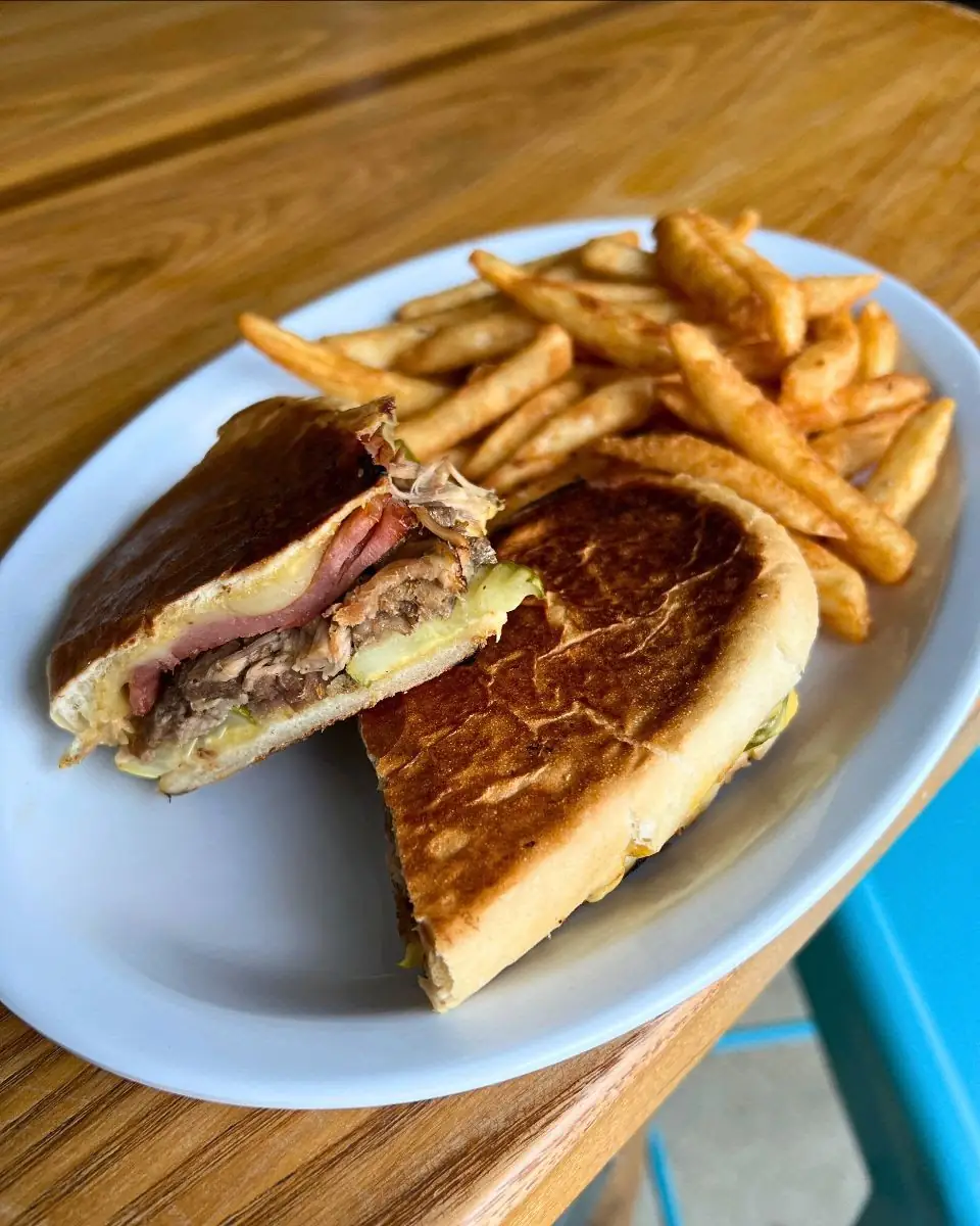 Image of a cubano sandwich cut in half with fries on a plate.