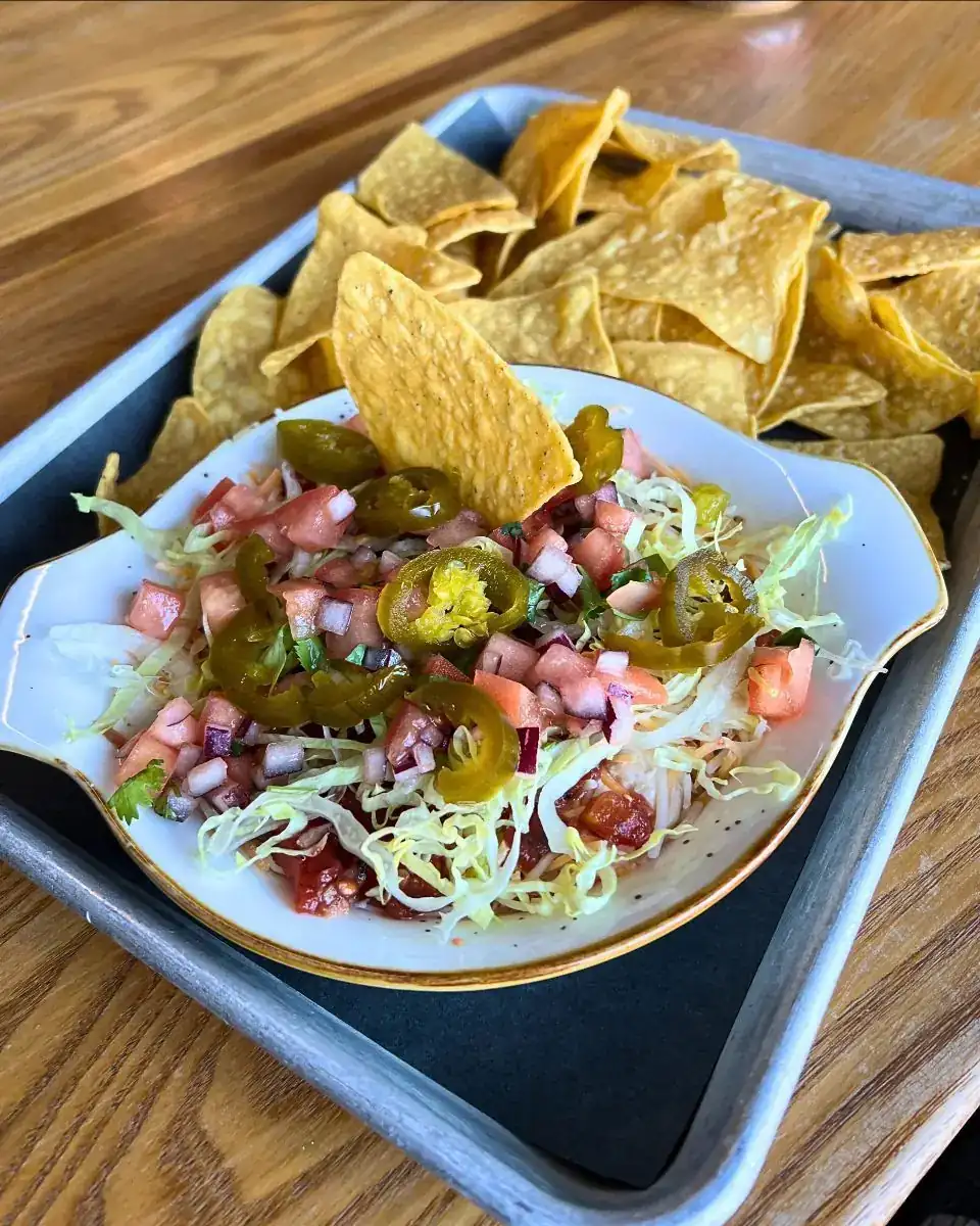 Image of a metal tray with tortilla chips on it and a white ceramic bowl with 7 layer dip.