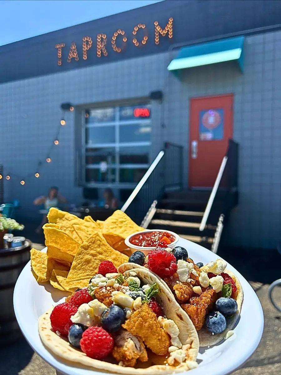 Two Mint Berry Crunch Tacos featuring crispy chicken, mint berry salsa, feta crumbles, and hot honey, served with tortilla chips and salsa on an outdoor patio