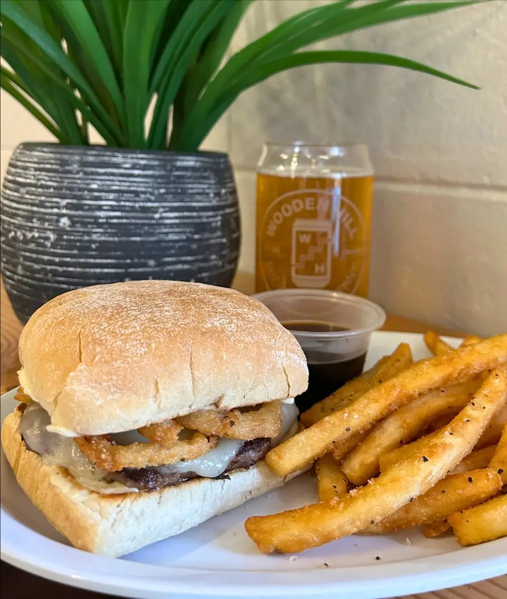 Angus beef French Dip Burger topped with provolone cheese, horseradish mayo, and crispy onion strings on a toasted ciabatta roll, plated with seasoned french fries and a side of au jus.