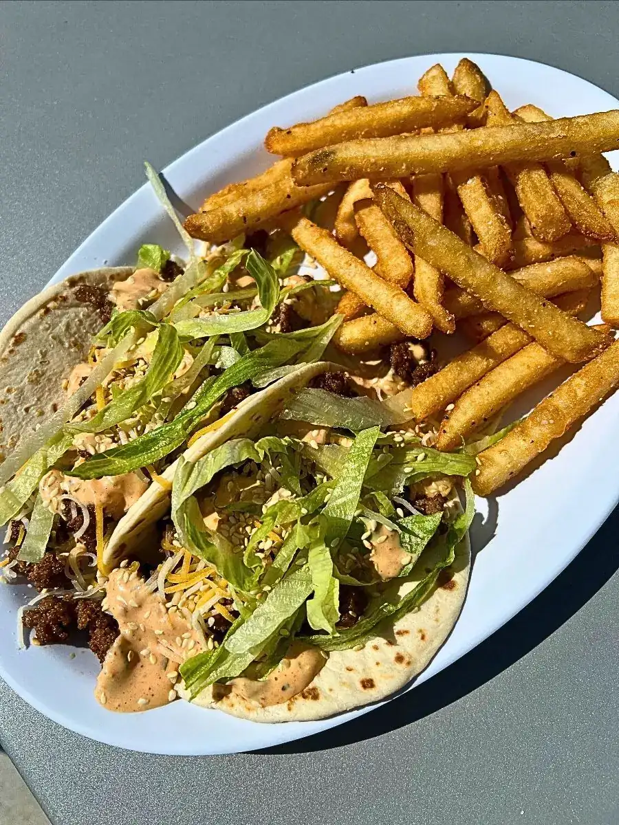 Taco Wednesday Special: Two soft tacos filled with seasoned ground beef, shredded cheese, lettuce, secret sauce, and sesame seeds, served with a side of crispy french fries.