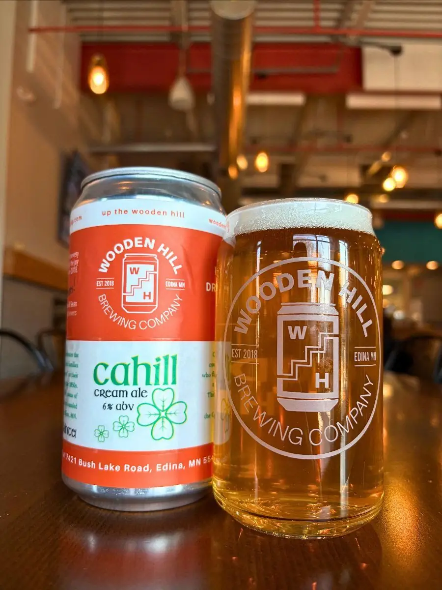 Image of a Wooden Hill Brewing can on the left with Cahill cream ale logo. Glass of a light beer on the right.