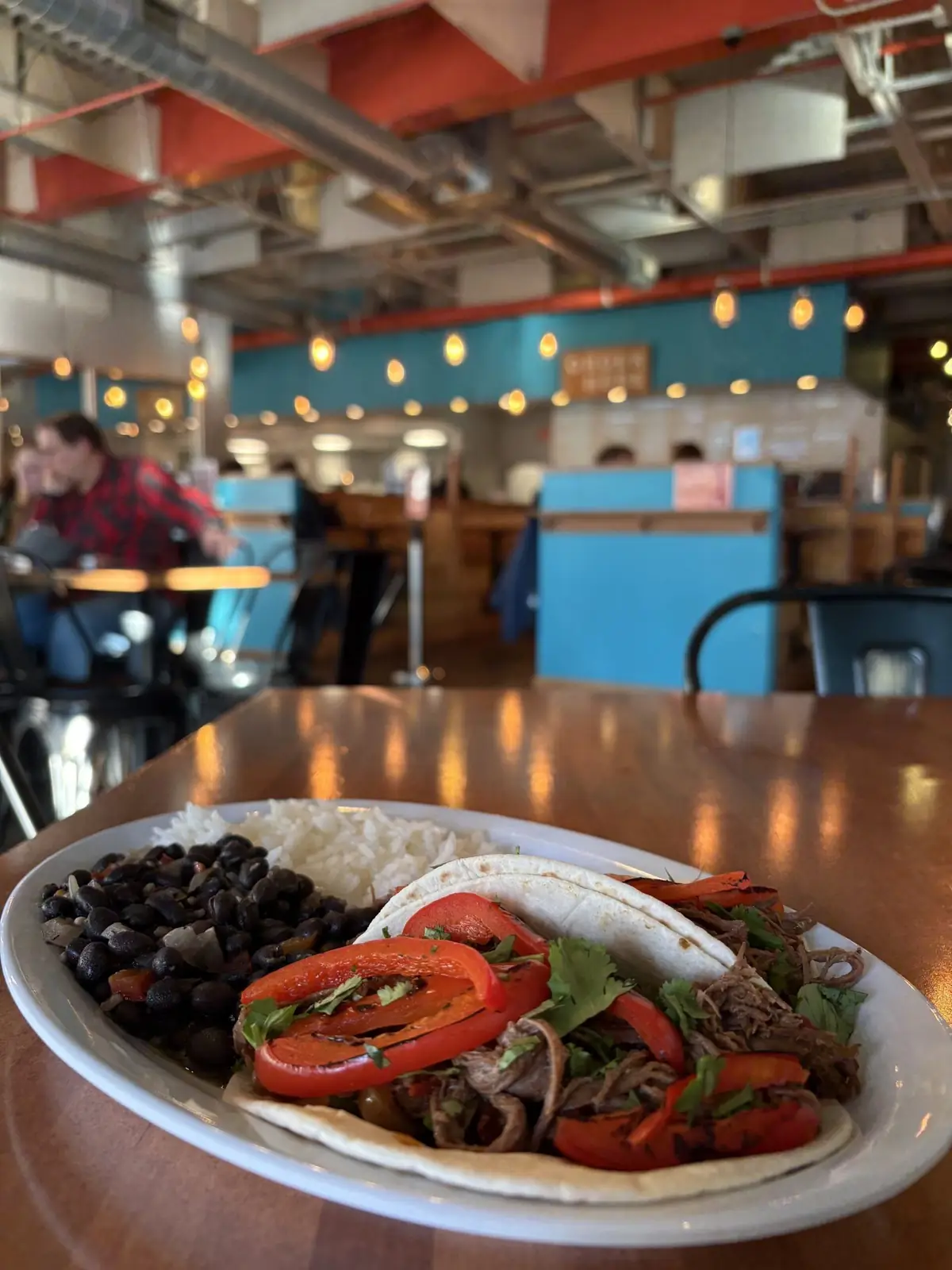 Image of ropa veja tacos on a plate with a side of beans and white rice. Background is inside Wooden Hill brewing.