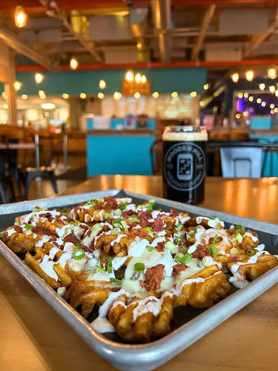 Image of Irish nachos on a platter with a Wooden Hill glass of dark beer in the background. Background of image is in a brewery.